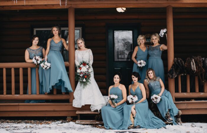 A bride and her wedding party posing on the front porch of a log cabin in the winter time