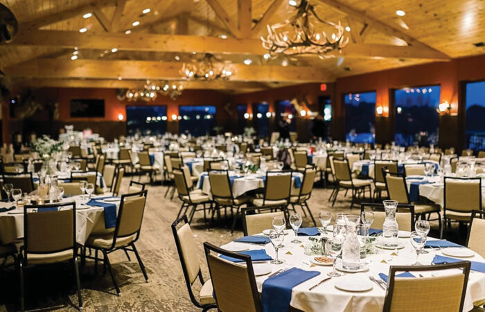 The grand lodge, filled with circular tables adorned with white table cloths. Deer antler chandeliers hang from the ceiling.