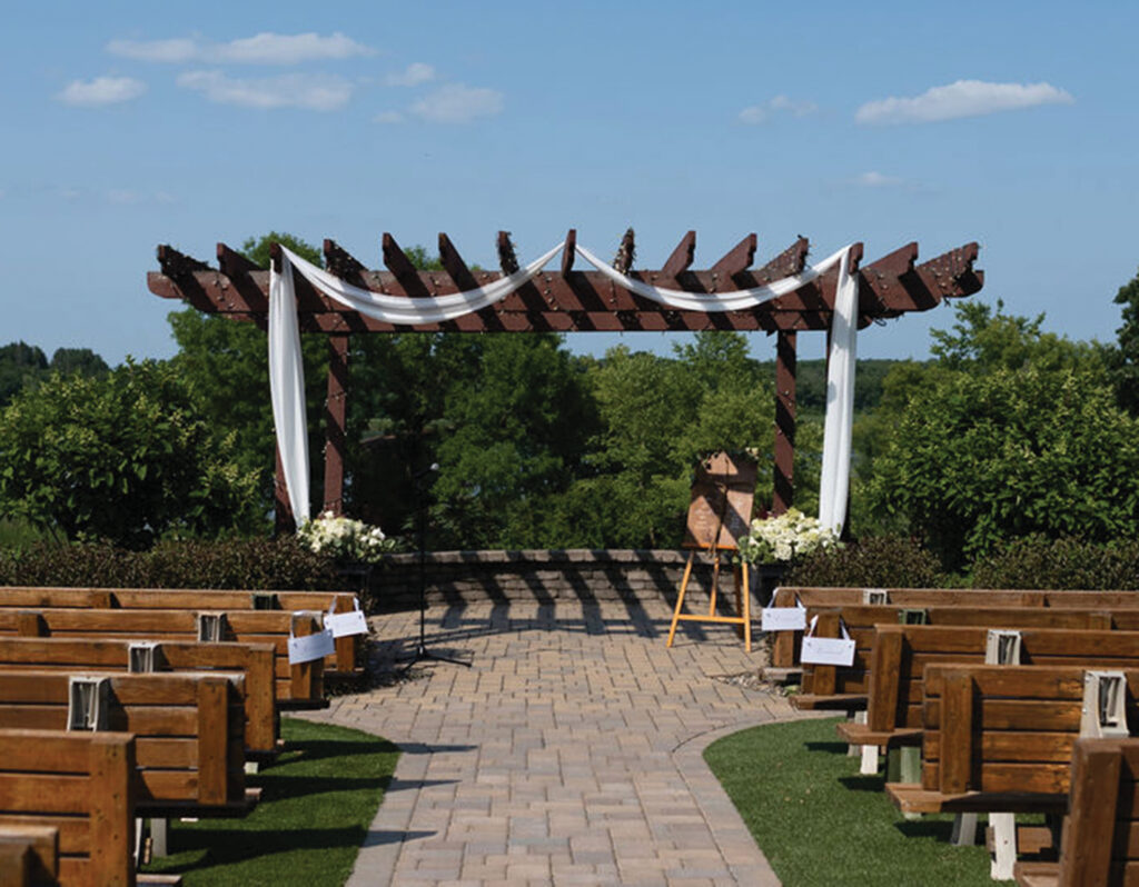 An arbor, adorned by wedding regalia, with benches on both sides of the aisle