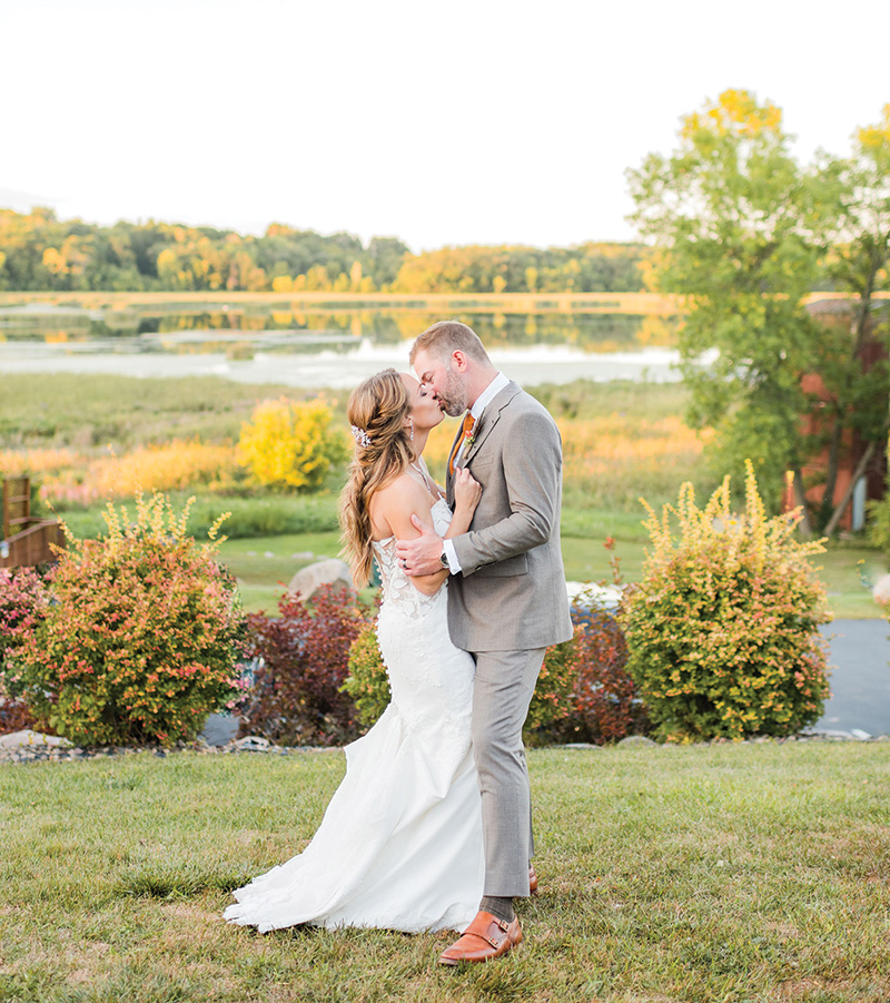 A newly-wed couple kissing with a gorgeous pond behind them