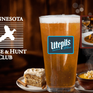 Glass filled with beer with piece of cake and soup near by.