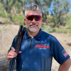 Portrait of Chad with sunglasses, blue shirt and shouldering a shotgun